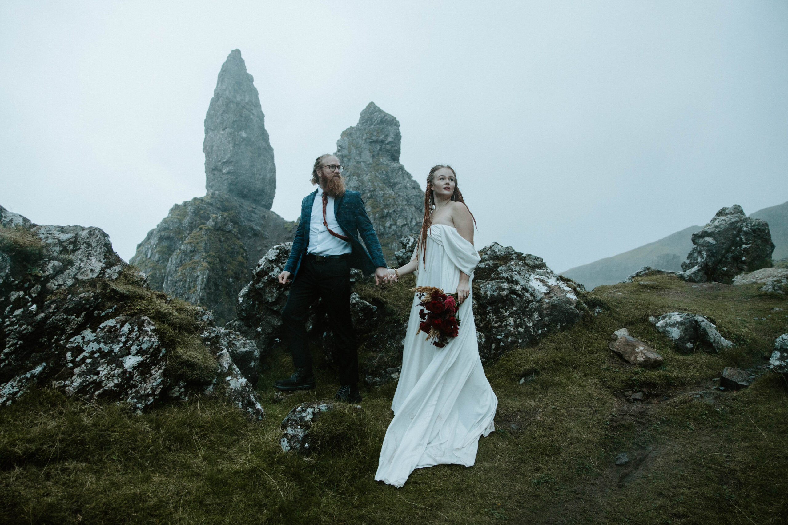 Couple holding hands with the dramatic rock formations of the Old Man of Storr in the background during their Scotland elopement.