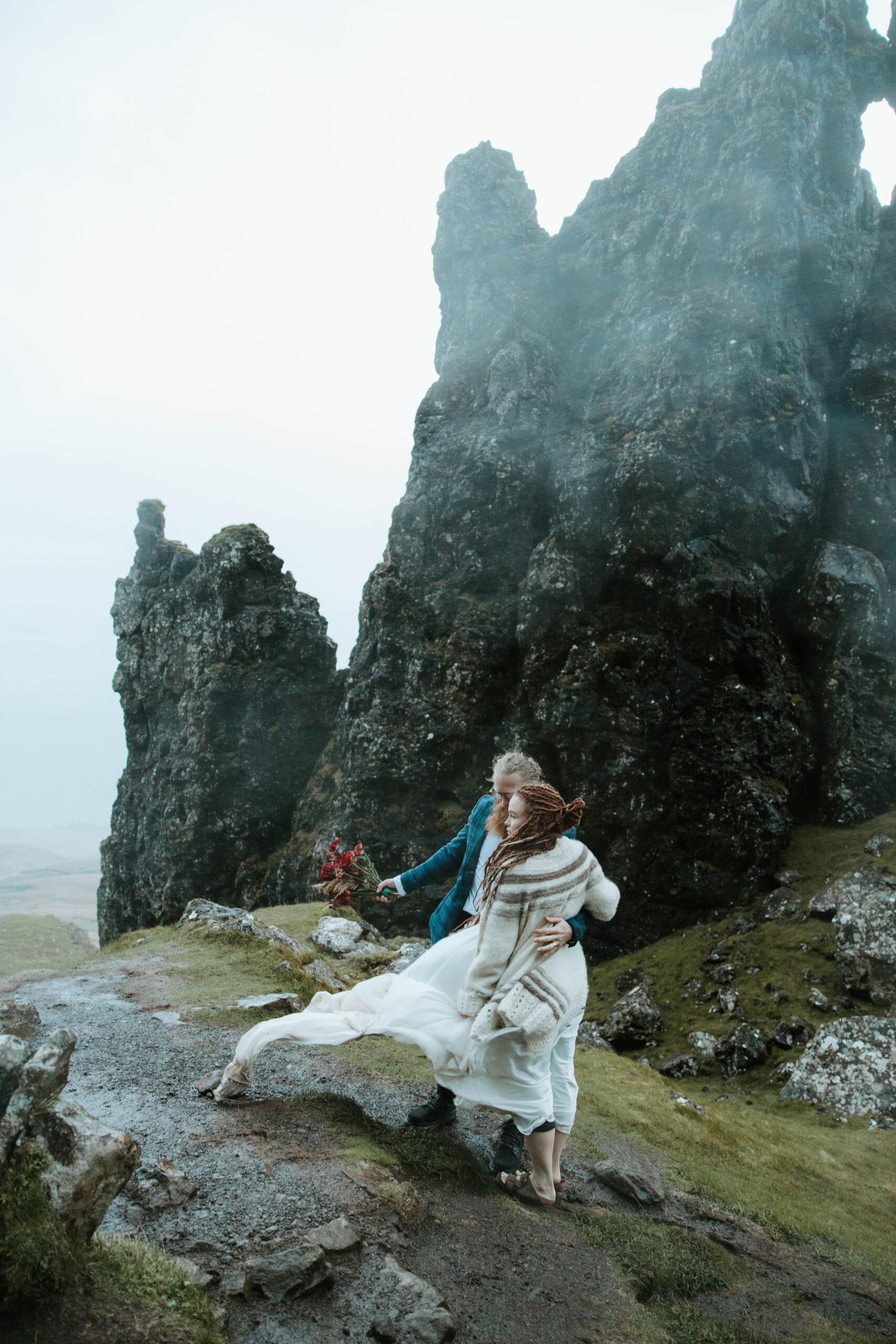 Eloping couple hiking up the rugged trail to the Old Man of Storr, surrounded by misty Scottish landscapes.