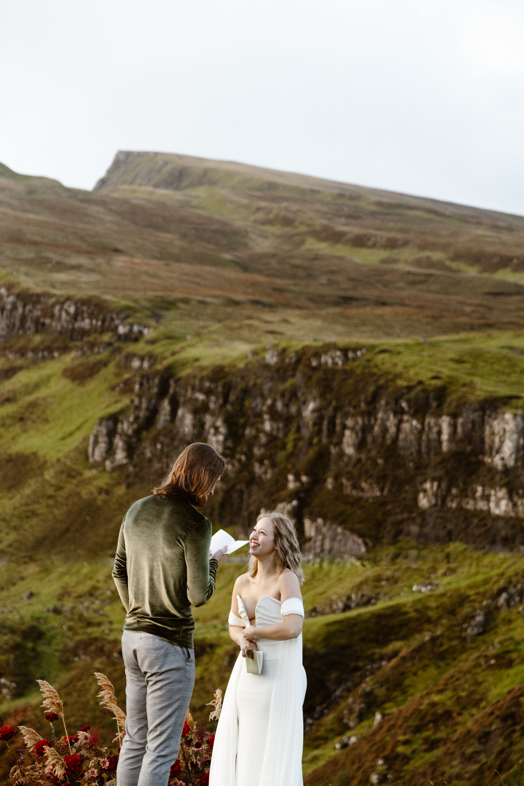 Couple reading vows together atop the Quiraing, overlooking the rolling green hills and unique rock formations of the Isle of Skye.