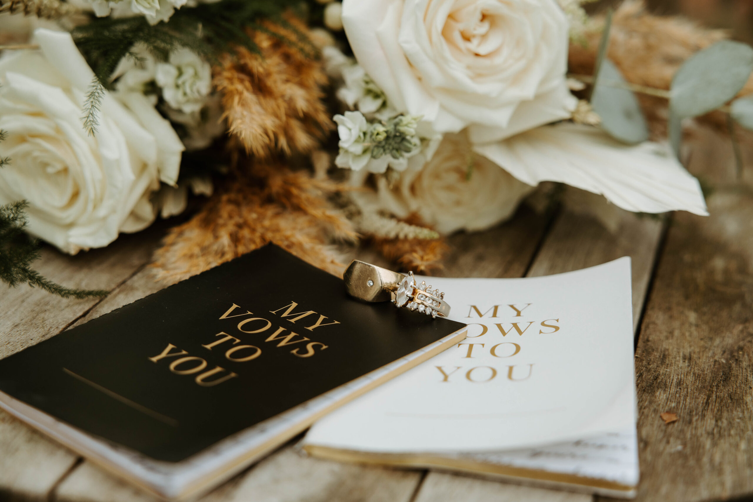 Close-up of elegant vow books with gold script lettering, wedding rings resting on top, symbolizing love and commitment at an intimate elopement.