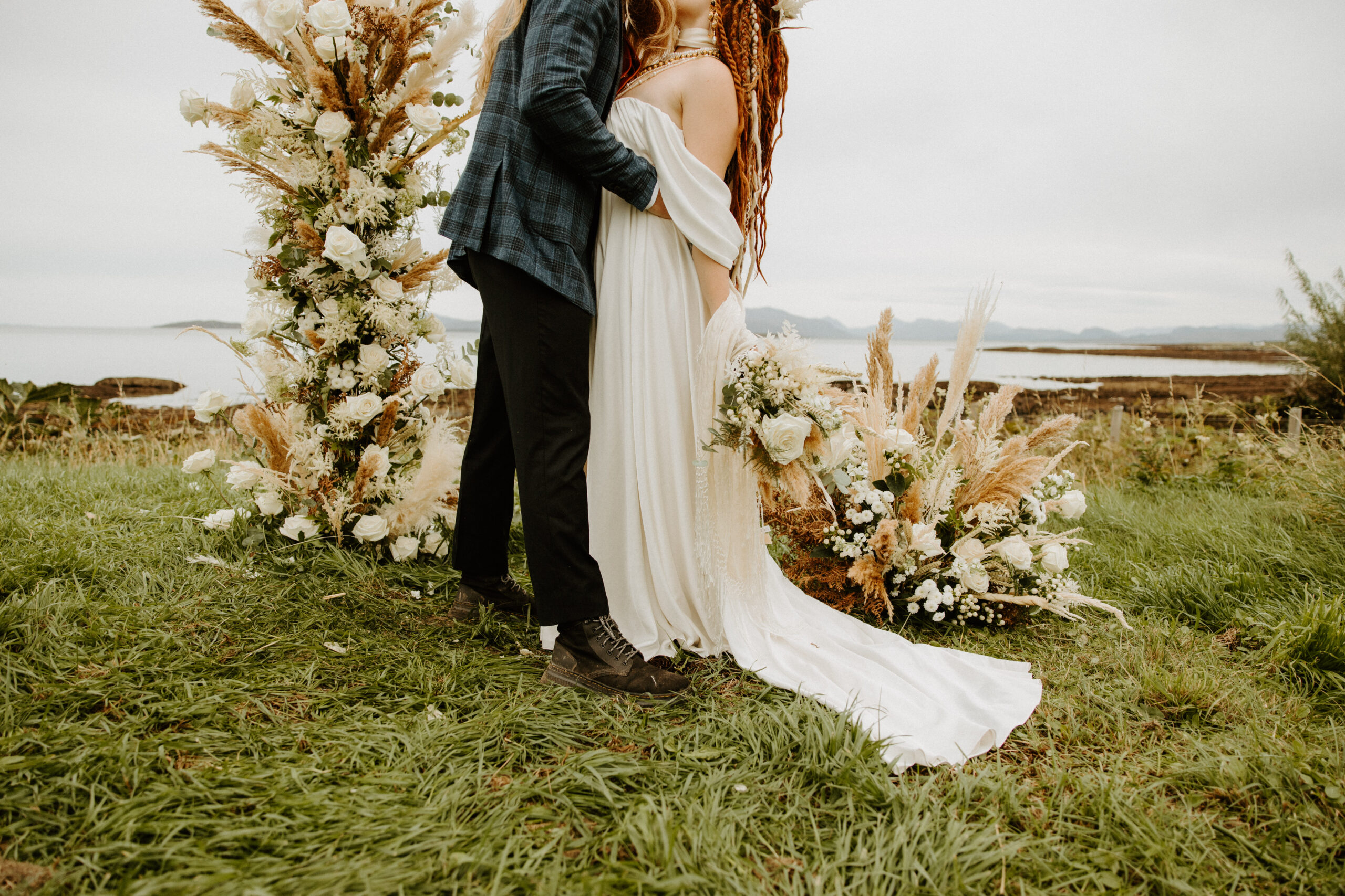 A couple sharing a romantic kiss on a scenic beach moments after saying 'I do,' with gentle waves and dramatic skies creating the perfect backdrop for their elopement.