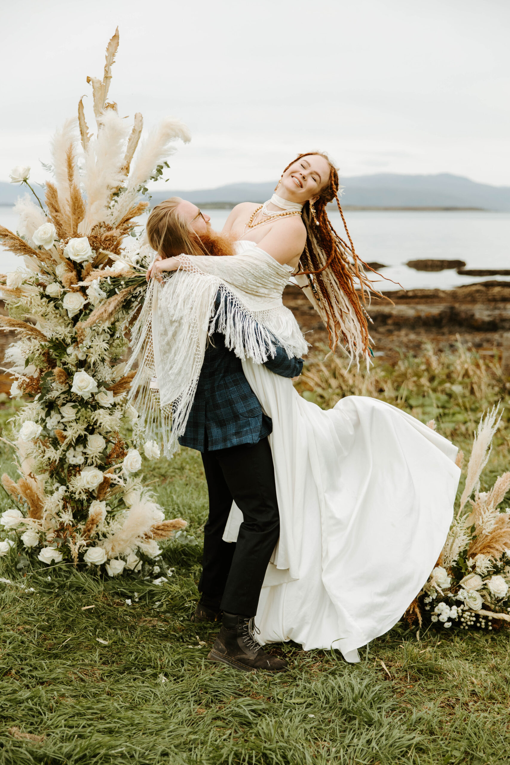 Eloping couple cuddling near rocky cliffs on the Isle of Skye's coastline, with dramatic waves in the distance.