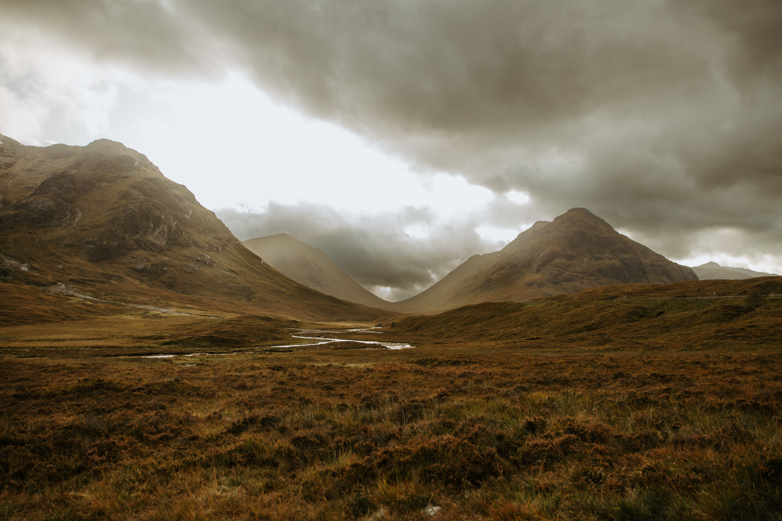 majestic peaks of Glencoe towering behind them under a cloudy Scottish sky.