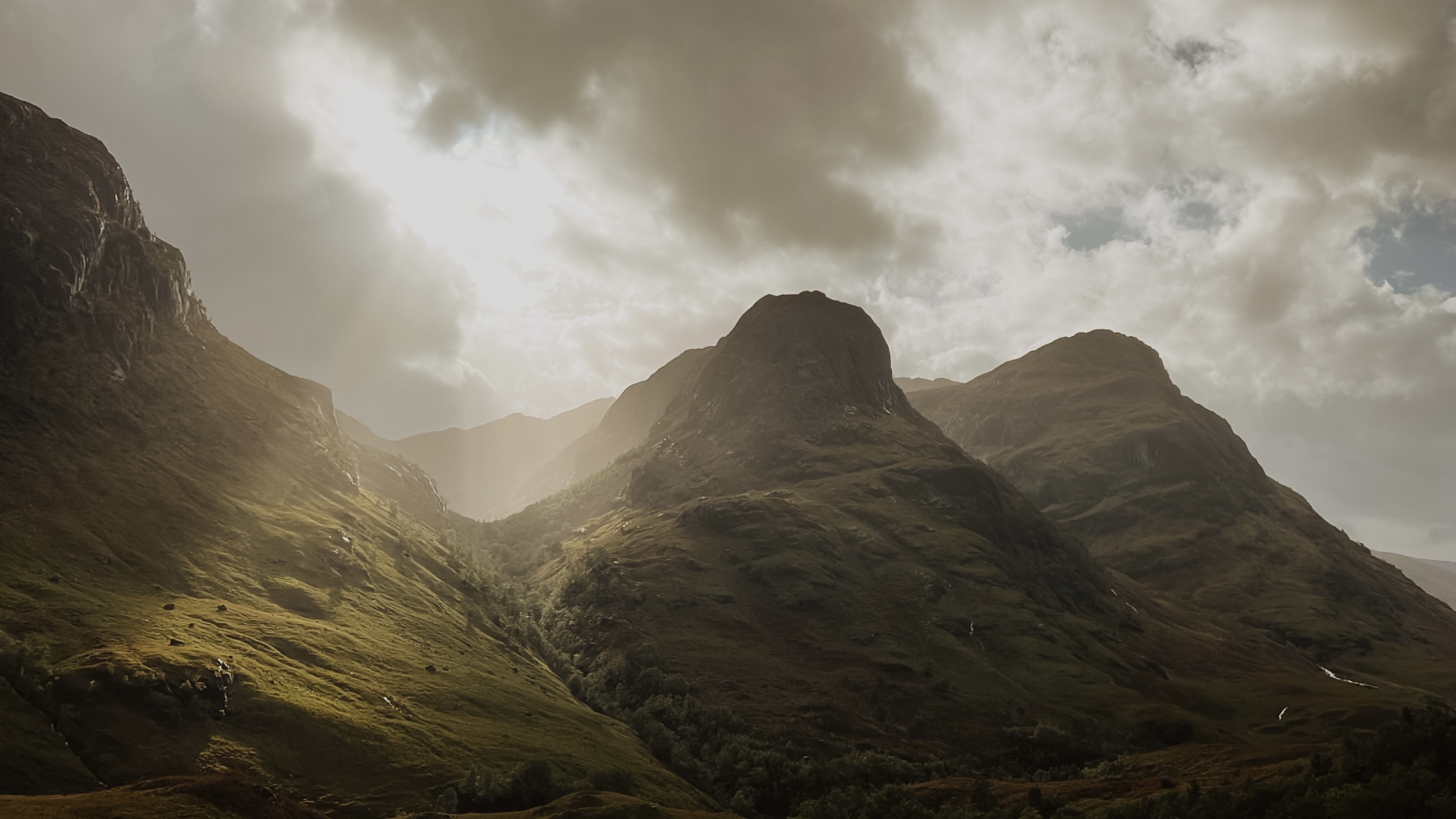 Eloping couple embracing with the majestic peaks of Glencoe towering behind them under a cloudy Scottish sky.