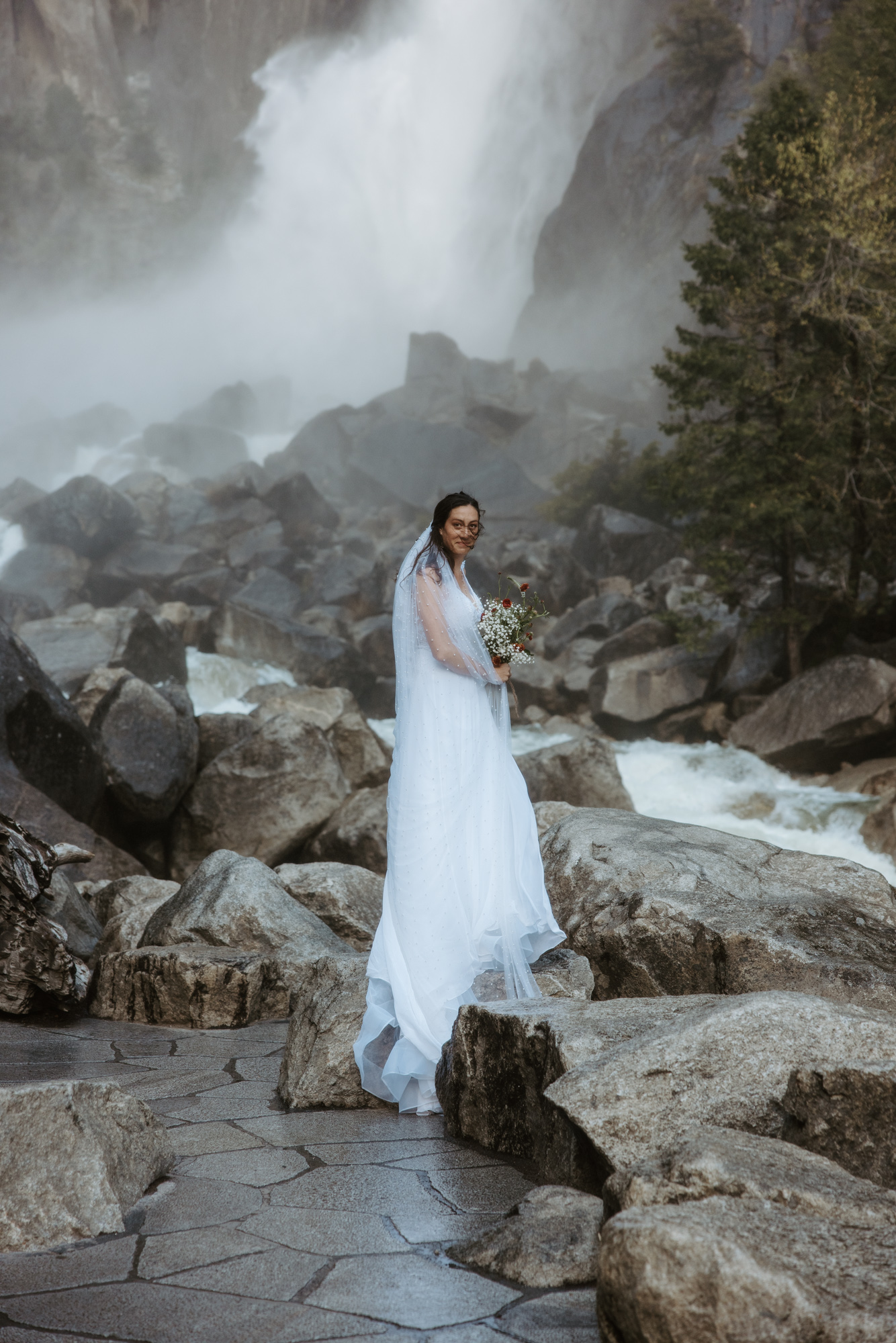 Bride standing near Yosemite Falls, feeling the mist on her skin — epic elopement experience in Yosemite National Park